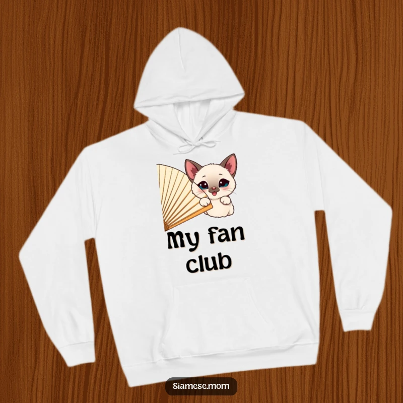 Funny happy Siamese cat peeking out from behind a large, cheerful fan, featured on a warm hoodie.