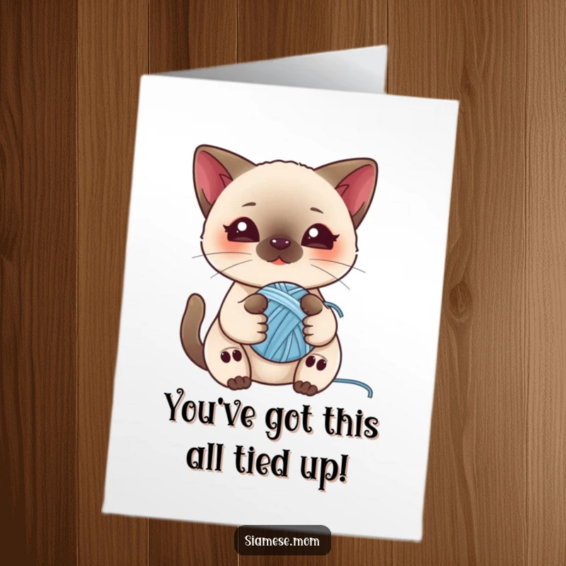Charming free printable congratulations card showing a kawaii Siamese cat happily clutching a small ball of yarn, full of playful spirit.