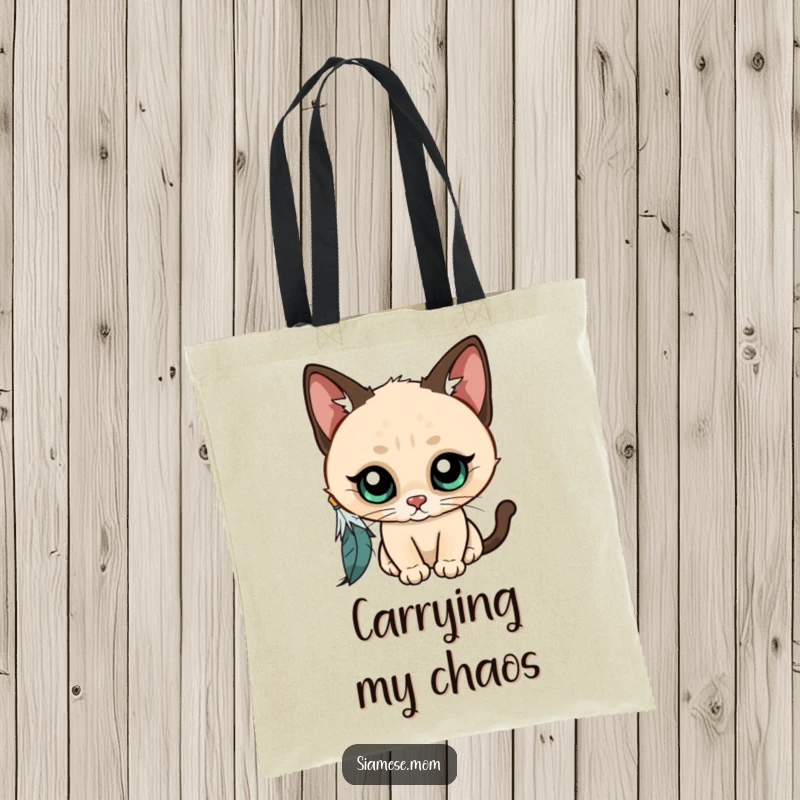Funny Kawaii Siamese cat tote bag, wide-eyed and curious, playfully batting at a dangling feather, a stylish and humorous accessory.
