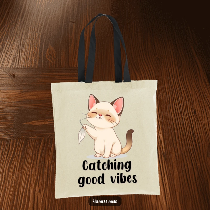 Funny Siamese Cat Tote Bag: A charming Siamese cat playfully swats at a descending feather, perfect for carrying fun essentials.