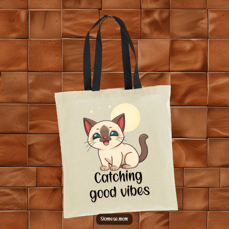 Funny stylized Siamese cat happily batting at glowing moonbeams, printed on a durable tote bag.